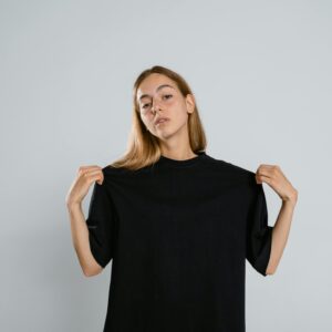 Teen girl in studio showing black T-shirt with arms raised against neutral background.